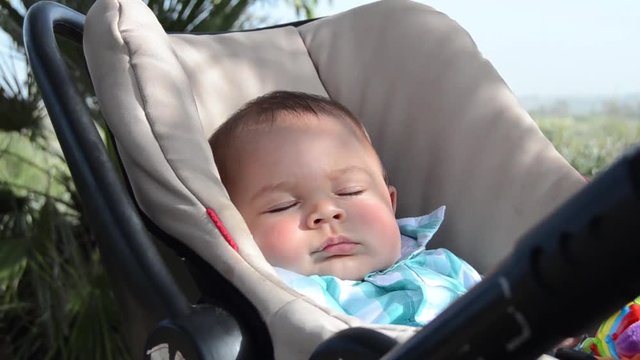 Cute six months old baby boy sleeping in the pushchair in the shadow of palm trees in the park Malta