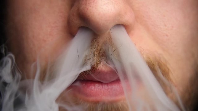Man exhales vapor through his nose in slow motion.