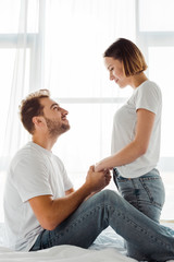 Obraz premium Happy couple holding hands and looking at each other in bedroom