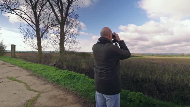 Footage of man looking at countryside with binoculars, this footage could show either a farmer looking over his fields, or a birdwatcher