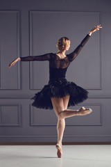 Ballerina dancer in black dress posing over gray background.