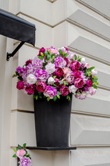 Artificial peony flowers in black vase on house facade
