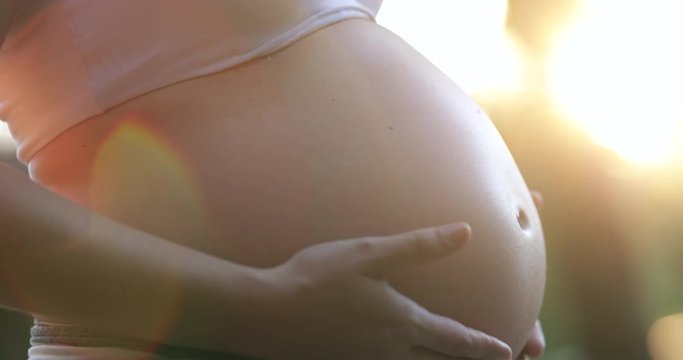 Pregnant woman expecting baby caressing belly outside with lens-flare sunlight