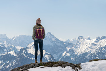 Girl with purple backpack standing on mountain peak looking to beautiful view over the european Alps in Austria.