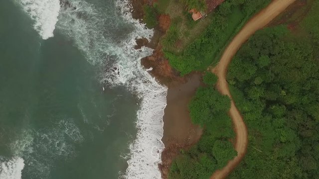 Aerial view of car driving on interesting dirt road between ocean waves and central american jungle. car drives top of scene to middle