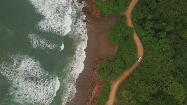 Aerial view of car driving on interesting dirt road between ocean waves and central american jungle. camera and car moves middle of scene to bottom