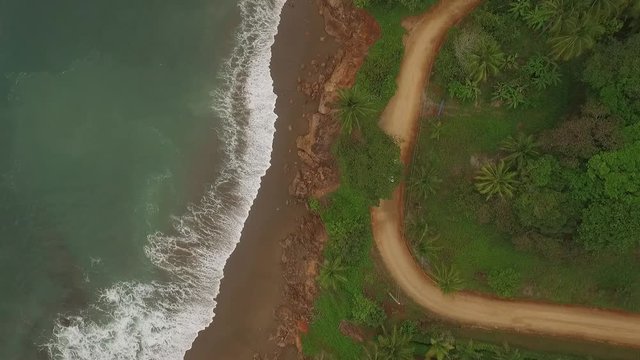 Aerial view of car driving on interesting dirt road between ocean waves and central american jungle moves bottom scene to top