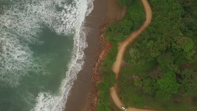 Aerial view of car driving on interesting dirt road between ocean waves and central american jungle. camera and car moves bottom of scene to exit right