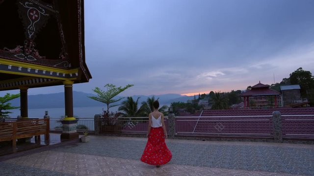 Woman in a red flowing skirt walking across the tile roof of a resort on Lake Toba in North Sumatra, Indonesia.