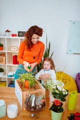 Red-haired mom showing her lovely girl how to water plants