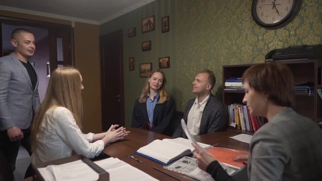 Caucasian Realtor Checking Documentation Needed For Contract in Office While Buyers Couple and Real Estate Brokers Waiting. Light Camera Movement