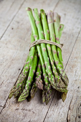 Bunch of fresh raw garden asparagus on rustic wooden table background. Green spring vegetables.