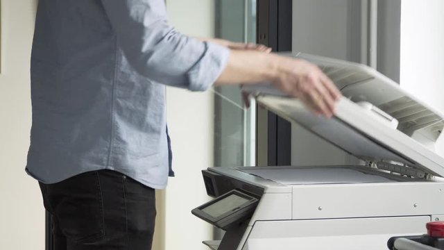 Caucasian worker man copying documents in the office. Close up young male at work in an office using the copy machine. Business documents concept.