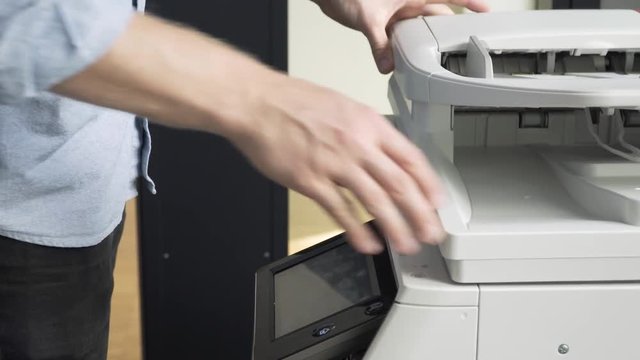 Close up Caucasian man copying documents in the office. Young worker male at work in an office using the copy machine. Business documents paperwork concept.