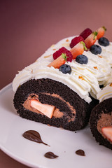 Chocolate roll cake with berries and fresh cream on brown background.