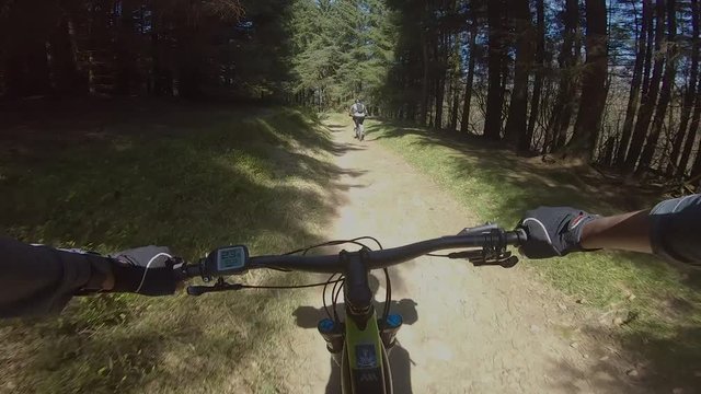 POV of cyclist on E Mountain Bike on trail with another cyclist in front in forest in the Peak District, UK