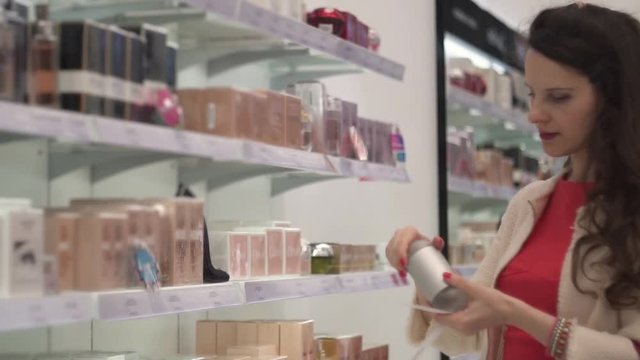 Glamorous attractive European woman brunette girl in red dress chooses perfume eau de toilette in supermarket, expensive perfume boutique, cosmetics and perfume shop, slow motion video
