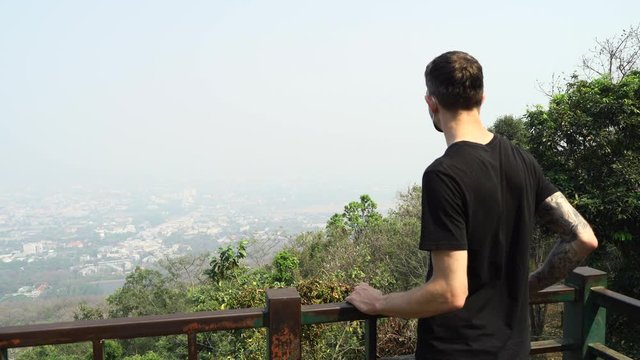Young man wearing a face mask checking the Chiang Mai cityscape view which is covered with high polluted air.