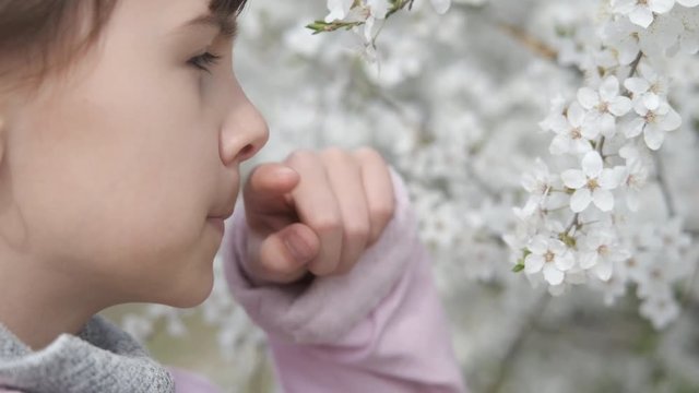 Allergic rhinitis. A young girl wipes her nose with her finger in the park during the spring blossom. Allergy to pollen.