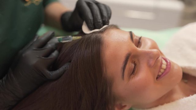Beauty expert dressed in black gloves growing hair for the beautiful brunett woman. Girl smiling and showing her perfect even teeth. Beayty concept