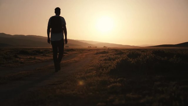 Steady shot of man walking on path towards the golden hour sun.