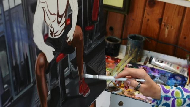 Female artist with colorful nails painting a portrait of a bodybuilder.