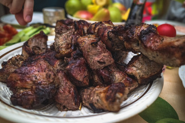 hand reaching for a piece of meat cooked on the grill and placed in a plate on the table with vegetables