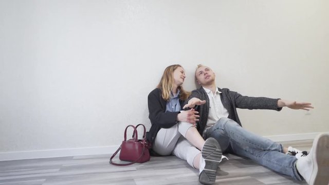 Casual Caucasian Young Married Couple Sitting on Floor of Empty Room of Their New Real Estate Apartment and Talking About Arragements