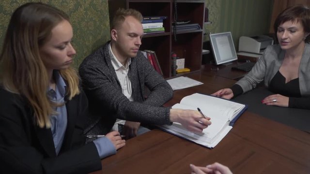 Male From Young Caucasian Couple Signing Contract in Office While Female Talking to Lawyers. Light Camera Movement