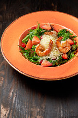 Fresh salad of arugula, shrimp and strawberry. Dark wooden background. Restaurant menu