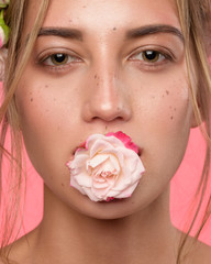Obraz na płótnie Canvas Beauty portrait of woman face with freckles and a rose flowers in a mouth. Beautiful blonde female spa model with perfect fresh clean skin looking at camera and smiling. Youth and Skin Care, florist
