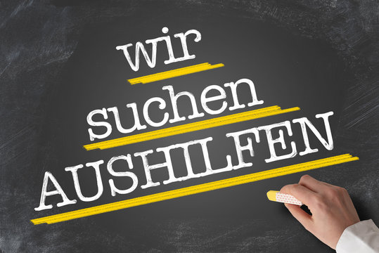 text WIR SUCHEN AUSHILFEN, German for Help Wanted, written on blackboard with hand holding piece of chalk