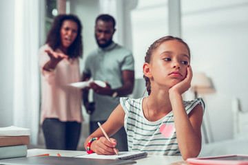 Bored girl studying while her parents discussing her bad academics.