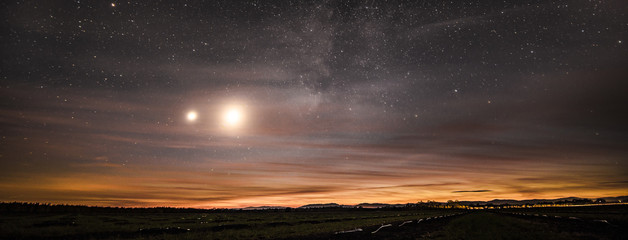 The moon, planet Venus, and the Milky Way galaxy shining through a thin layer of clouds at dusk, over an agricultural field in Northern California © Photography by Adri