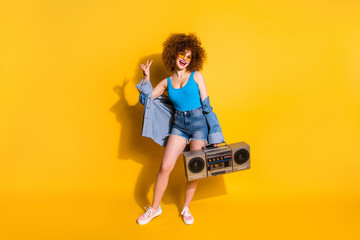 Full length body size photo beautiful she her lady wavy styling curls old-fashioned tape recorder show v-sign wear specs casual jeans denim shirt shorts tank top clothes isolated yellow background
