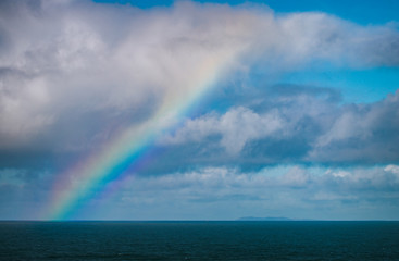 A rainbow breaks through the clouds over the ocean, on a cloudy day on the Northern California coast, near San Francisco. 