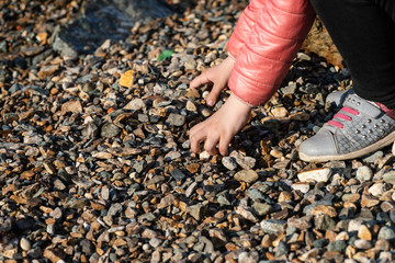 Little girl at rocky beach playing with pebbles.
