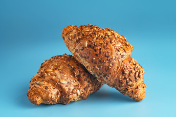 Photo of fresh golden croissants covered sunflower seeds and sesame captured on blue background.
