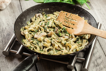 Tagliatelle pasta with spinach and mushrooms on a pan.