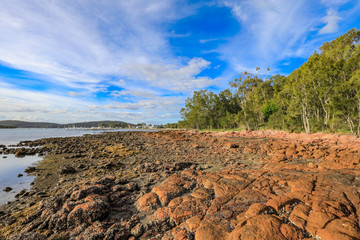 Rocky coastline at low tide leading to cloudy sky and marina