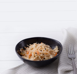 Fermented cabbage. Traditional russian appetizer sauerkraut with carrot in craft plate on white wooden table.
