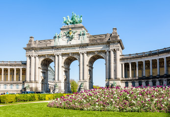 Fototapeta na wymiar The arcade du Cinquantenaire, the triumphal arch erected by king Leopold II in the Cinquantenaire park in Brussels, Belgium, with a flowerbed in full bloom in the foreground against blue sky.