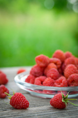 Pink fresh raspberries on an glass vessel on a gray wood background in the garden on the background of green grass Berry Fruit Sadovina Healthy Food hack close up