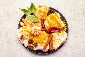 Raw chicken thighs with traditional indian spices. Yellow curry mix, star anise, cardamom, bay leaf, pepper, garlic, cinnamon. Ingredients for cooking on a stone background, close up, top view.