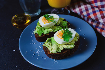 Healthy healthy snack (breakfast) - a sandwich with avocado and egg on a gray plate and a glass of fresh orange juice.