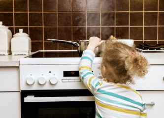 Accident waiting to happen. Toddler girl pulling boiling pot of water over in home kitchen. Hazard...
