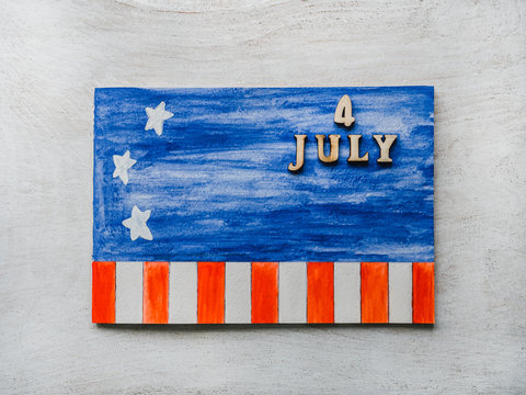 4 JULY. Notepad, American flag drawing and wooden letters of the alphabet on a white table. Close-up. Bright photo and space for your inscriptions. Congratulations to relatives, friends and colleagues