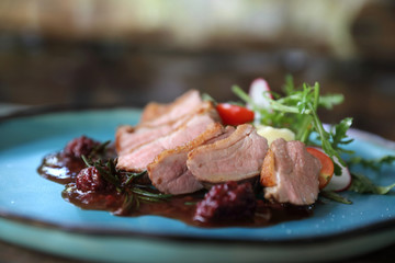 Duck confit with salad , baked apple and raspberry sauce served on wooden table