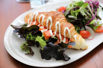 Croissant bread with salmon and salad on wooden background