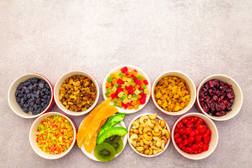 Dried and candied fruit and cashew nuts. Assorted in ceramic bowls on a stone background. Healthy vegetarian (vegan) food concept, copy space, top view.